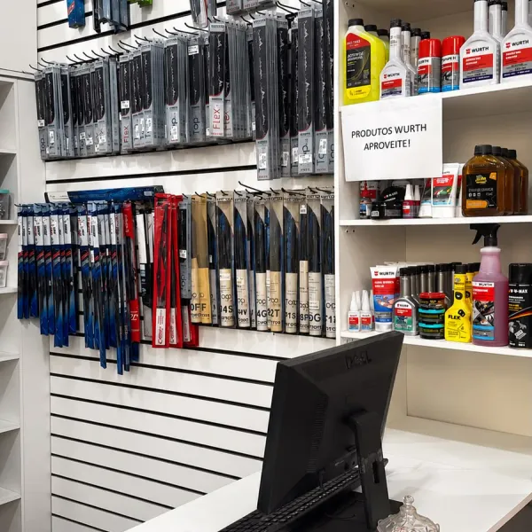 Balcão de atendimento da loja, com computador e maquininha de cartão, ao lado da parede de palhetas de limpador e da prateleira de produtos Würth