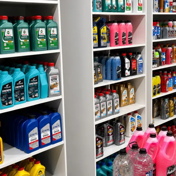 Prateleiras brancas com óleos de motor Castrol, Mobil, Repsol e Atron e galões cor-de-rosa de aditivo de radiador